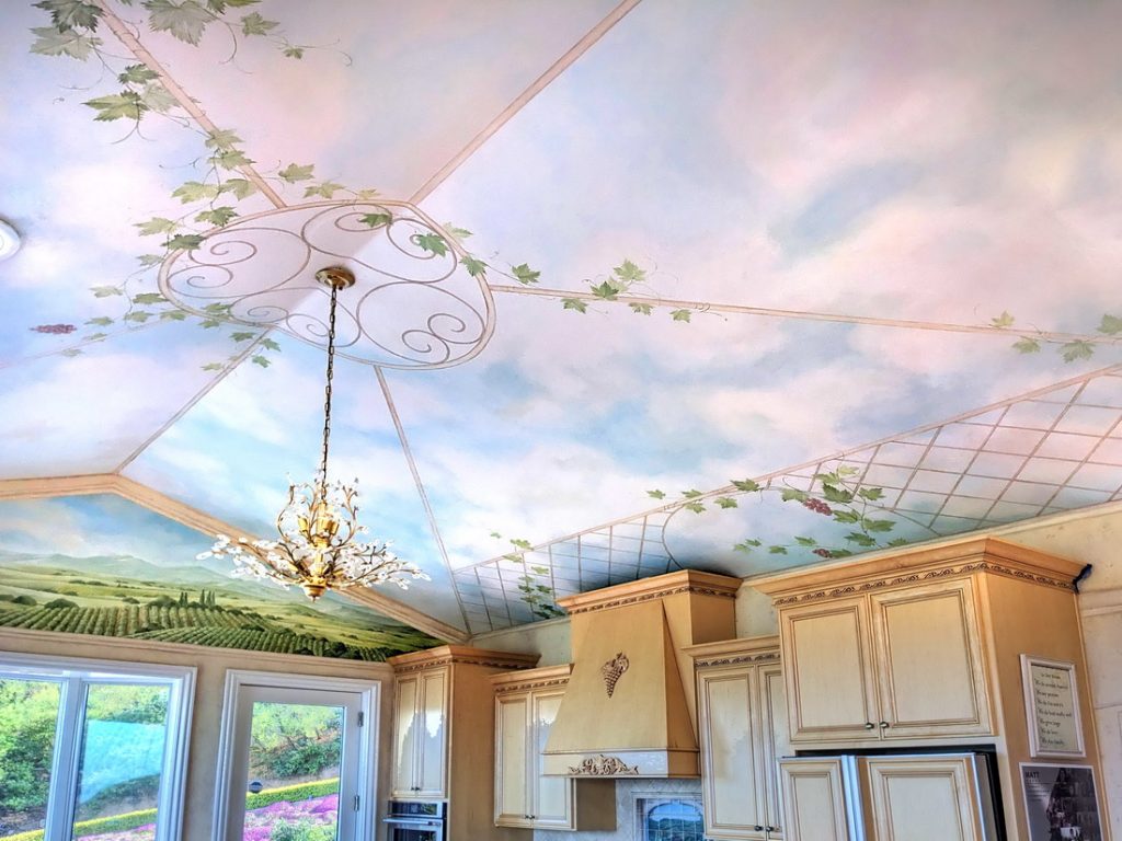 Private kitchen mural by residential mural artist Yulia Avgustinovich in California, featuring a painted sky ceiling with grapevines on a trellis and views of Italian vineyard landscapes