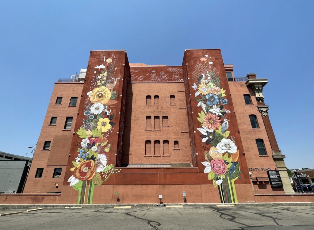 Large-scale symbolic mural by public art mural artist Yulia Avgustinovich in downtown Boise, Idaho, featuring Idaho state symbols, cultural heritage, and historic elements.