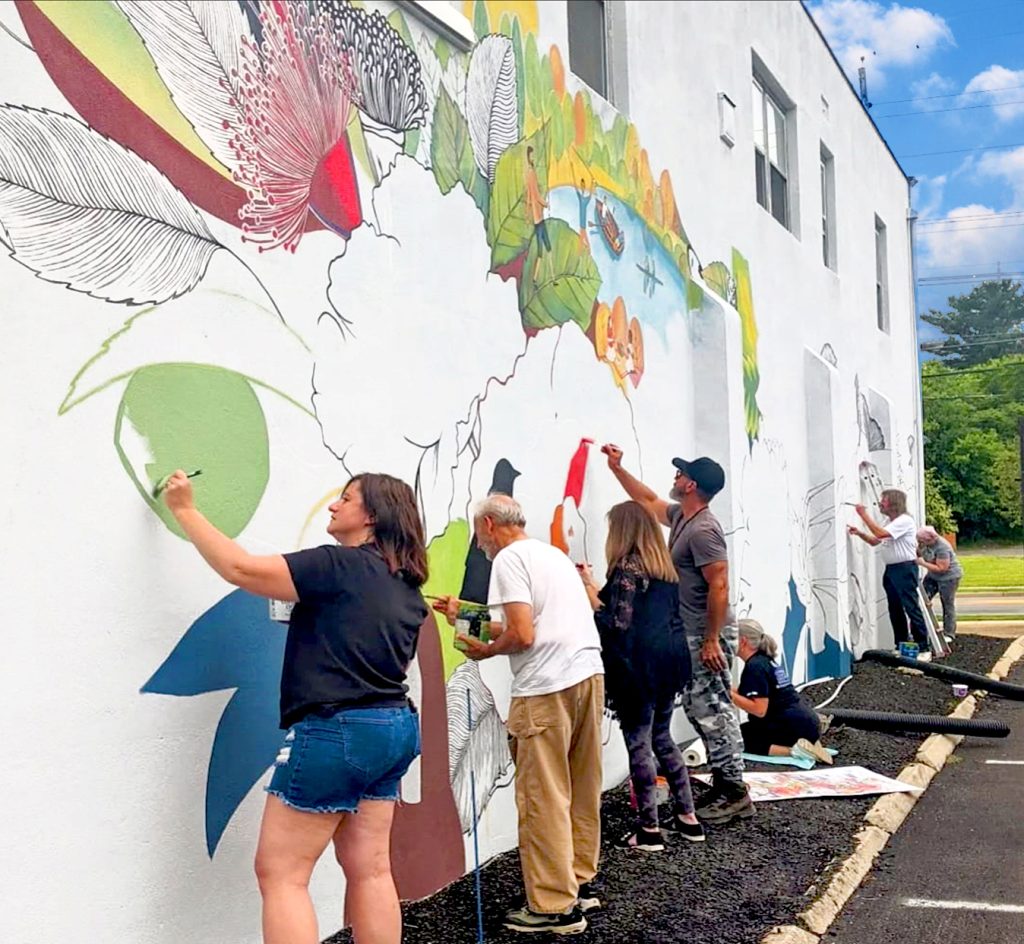 community-mural-painting-process-yulia-avgustinovich-runnemede-nj Community members painting a floral mural by Yulia Avgustinovich on the exterior wall of a flower shop in Runnemede, New Jersey.