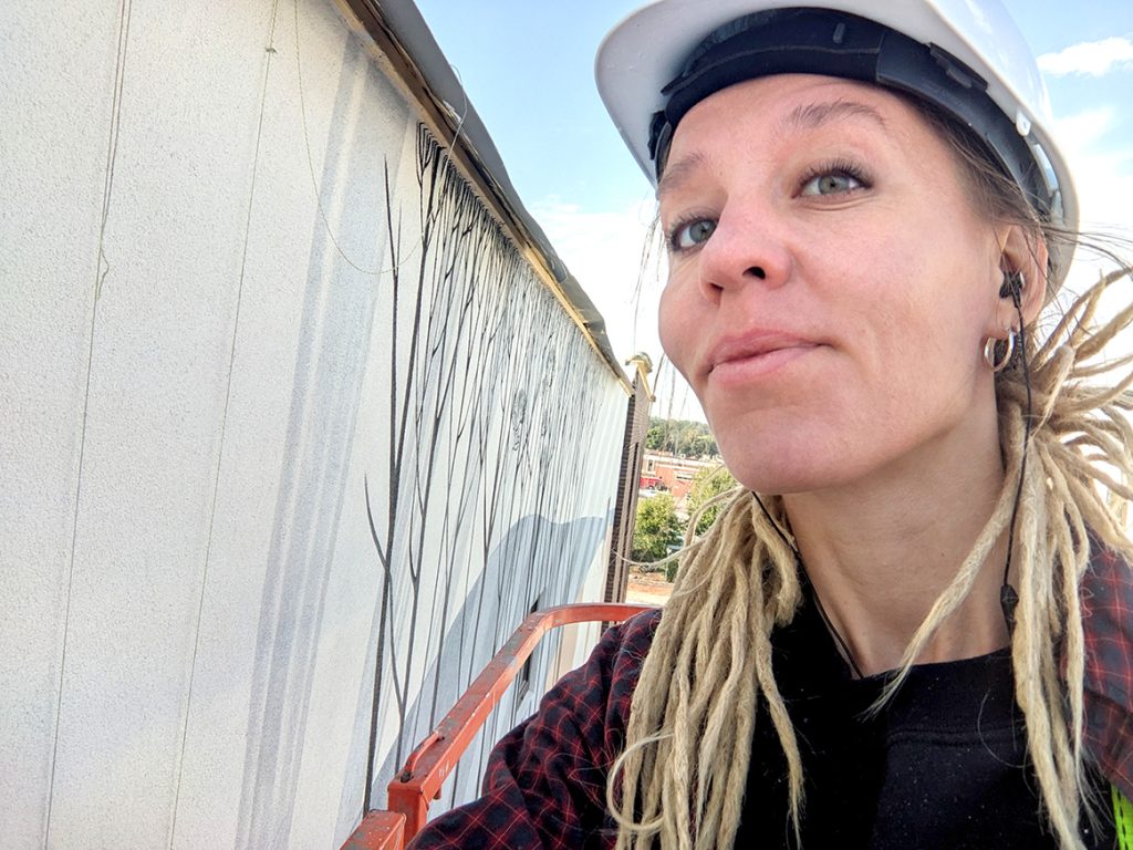 Artist Yulia Avgustinovich painting large-scale mural using boom lift in Caldwell Idaho