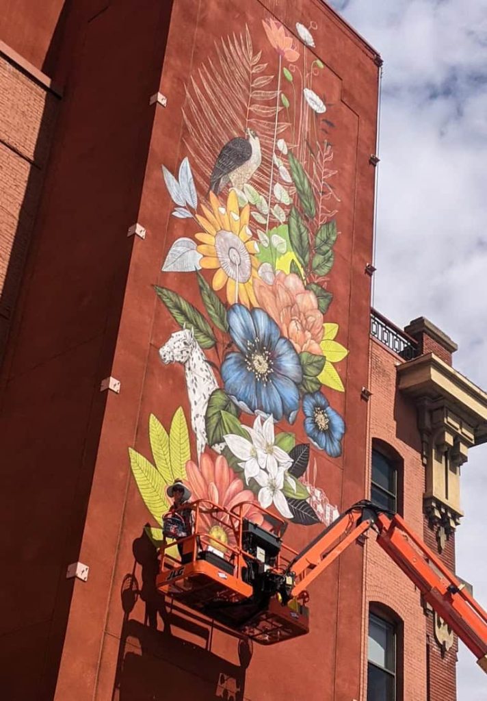 Artist painting symbolic public mural in downtown Boise using a lift