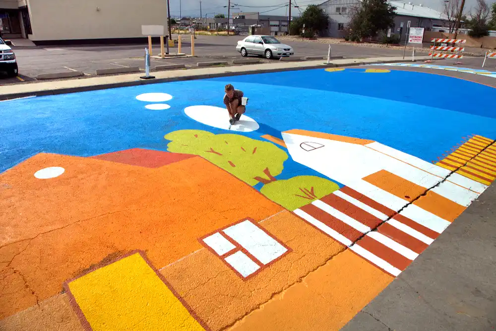 Close-up detail of painted asphalt mural showing graphic elements and street-marking paint texture with artist Yulia Avgustinovich painting