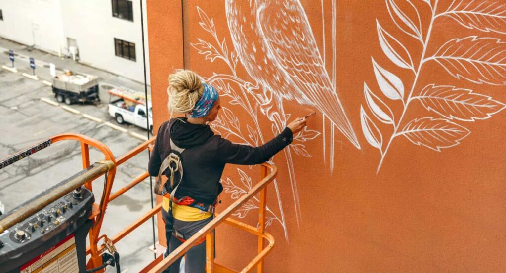 Artist painting symbolic public mural in downtown Boise using a lift